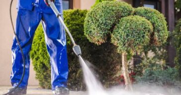 Caucasian Worker in His 30s with Pressure Washer Cleaning Residential Driveway. Garden and Home Surrounding Maintenance.